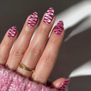 A close-up of a hand with manicured nails painted in a pink and white zebra stripe pattern, wearing a gold ring and a pink knit sleeve against a dark gray background with soft light shadows, Obroi