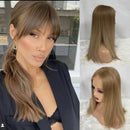A woman modeling a straight medium-length wig with bangs, shown alongside two smaller views of the wig on a mannequin head from the back and side. The wig has a warm light brown/blonde tone, Obroi
