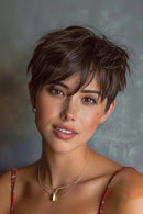 A close-up portrait of a woman with a short, textured dark brown pixie cut, wearing a red spaghetti-strap top and gold necklaces against a textured gray background, Obroi