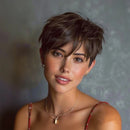A close-up portrait of a woman with a short, textured dark brown pixie cut, wearing a red spaghetti-strap top and gold necklaces against a textured gray background, Obroi