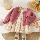 Floral dress with pink cardigan and white shoes on a textured surface, Obroi