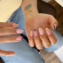 Close-up of hands with pink and gold nail polish, wearing a blue denim shirt, Obroi