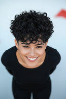 Woman with short, curly black hair against a light blue background, Obroi