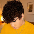Person with short, curly hair wearing a yellow sweater indoors, Obroi