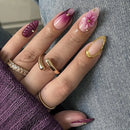 Close-up of a hand with decorative nails and gold rings on a textured surface, Obroi