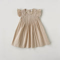 A light beige baby dress with flutter sleeves and vertical smocking on the bodice, laid flat against a light gray background, Obroi