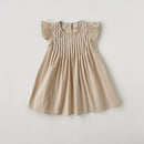 A light beige baby dress with flutter sleeves and vertical smocking on the bodice, laid flat against a light gray background, Obroi