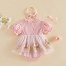 A pink baby girl's dress set laid flat on a warm beige background, including a pink gingham romper with puff sleeves, a layered tulle skirt with floral embroidery and lace, a matching bow headband, and a small ribbon bow, Obroi