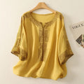 Yellow blouse with intricate patterns on a hanger against a white background, Obroi