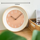 Round wall clock with a peach-pink face, white inner ring, and light wood frame, shown on a tabletop with a dimension label reading 30cm/11.81inch above it, Obroi