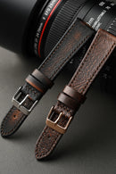 Two brown leather straps with metal buckles on a dark surface, Obroi