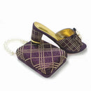 A pair of purple and gold plaid high-heeled mule sandals shown with a matching plaid handbag and pearl chain strap on a white background, Obroi