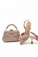 Rose gold handbag and high-heeled shoes with floral details on a white background, Obroi