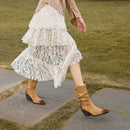 Person wearing a beige lace dress and brown boots walking on a stone path with grass, Obroi