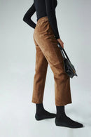 Person wearing brown corduroy pants and black top, holding a black handbag on a light gray background, Obroi