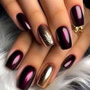 Close-up of hands with dark purple and gold nail polish on a soft surface, Obroi