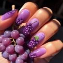 Nails with grape design held next to real grapes, Obroi