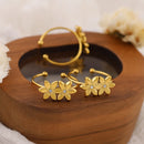 Gold floral earrings on a wooden surface with a soft background, Obroi