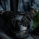 Person wearing black gloves holding a black motorcycle helmet with 'Motor' branding, Obroi
