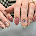 Close-up of hands with pink nail polish and floral designs on a blurred background, Obroi