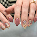 Close-up of hands with pink nail polish and floral designs on a blurred background, Obroi