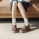 Person wearing brown shoes and white socks sitting on a beige couch, Obroi