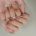 Hand with stylish nail design featuring gold accents on a neutral background, Obroi