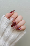 Nails with a gradient design in red and pink, held by a person wearing a white textured sleeve, Obroi