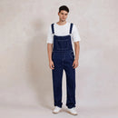 Person wearing blue denim overalls and white sneakers on a plain background