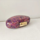 Oval-shaped purple and gold compact on a white surface, Obroi