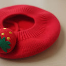 Red knitted beret with a strawberry decoration on a light wooden surface, Obroi