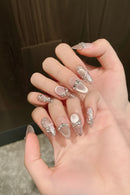 Hand with decorative nails featuring pearls and crystals on a blurred background, Obroi