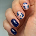 Hand with blue and floral nail design on a neutral background, Obroi