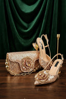 A coordinated women's fashion set featuring a pair of pointed-toe high-heel sandals and a matching clutch bag, both covered in shimmering rose-gold sequins with large 3D floral embellishments and gold-tone chain details. The set is displayed on a dark wooden table in front of a dark green velvet curtain backdrop, Obroi