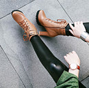 Person wearing brown high-top sneakers and black leggings on a gray pavement, Obroi