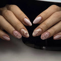 Close-up of hands with decorative nail art in front of a black background, Obroi