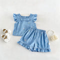 A baby girl's two-piece outfit set in light blue denim, featuring a ruffle-sleeve top and matching ruffled shorts with small embroidered flowers and butterflies. The outfit is styled in a flat lay with white baby shoes and a pearl beaded purse on a light beige background, Obroi