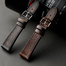 Two brown leather watch straps on a dark surface with a camera lens in the background, Obroi