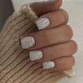 Close-up of a hand with glittery silver nail polish wearing a beige knitted sleeve, Obroi