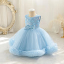 A light blue toddler girl's party dress displayed on a mannequin torso. The sleeveless dress features a floral lace bodice, a matching blue satin waistband with a large bow, and a voluminous tulle skirt with a ruffled hem, Obroi