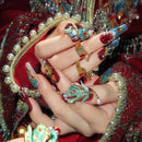 Close-up of hands with ornate nail art and jewelry against a red and gold embroidered fabric background, Obroi