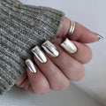 Hand with silver nail polish wearing a textured gray sleeve, Obroi