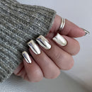 Hand with silver nail polish wearing a textured gray sleeve, Obroi