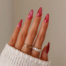 Close-up of a hand with red nail polish and multiple rings on a neutral background, Obroi