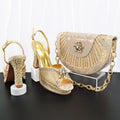 Gold high-heeled shoes and matching handbag on a black surface with white background, Obroi