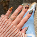 Hand with intricately designed nails, wearing a textured sleeve and ring, against an outdoor background, Obroi