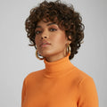 Woman with curly hair wearing gold hoop earrings and an orange turtleneck sweater, Obroi