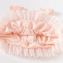 A pale peach pink ruffled baby bonnet with satin trim and matching bow details, photographed on a clean white background, Obroi