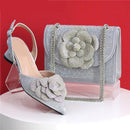 Silver high-heeled shoe and matching handbag with floral embellishments on a red background, Obroi