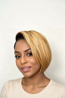 A woman wearing a short, layered bob wig with blonde highlights and dark roots, shown against a plain light background, Obroi
